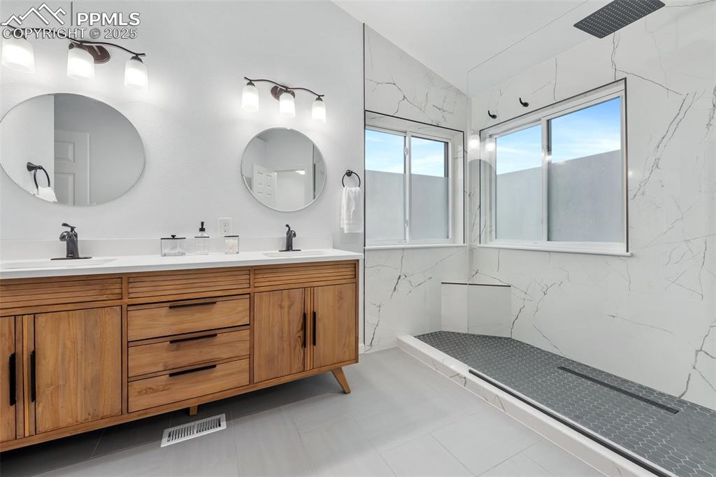 Image 24 of 44: Bathroom featuring double vanity, a marble finish shower, and lofted ceilin