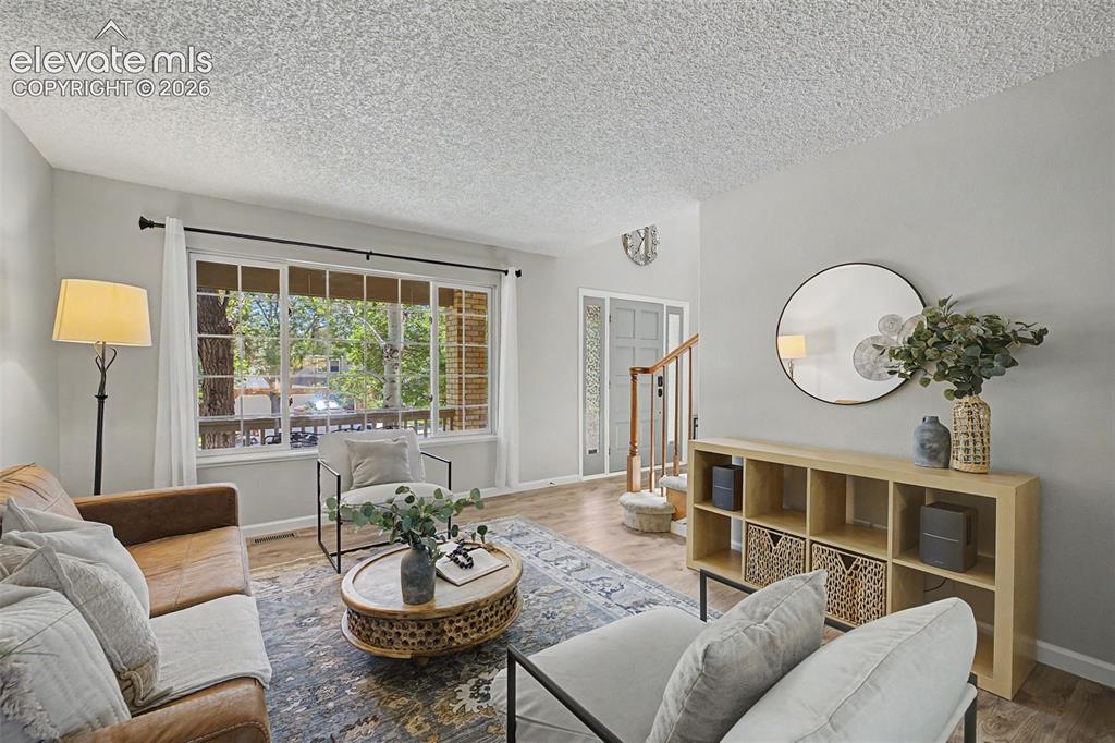 Image 12 of 49: Bright living area featuring wood-finish flooring, a large multi-pane windo