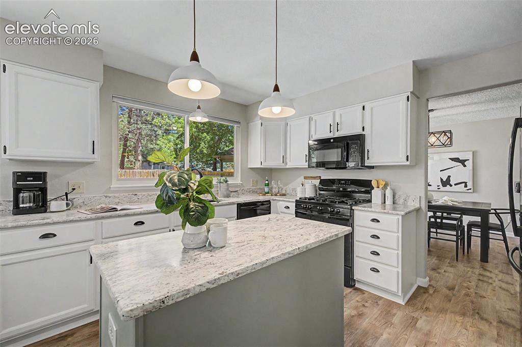 Image 20 of 49: Bright kitchen featuring a central island with a stone-finish countertop, w