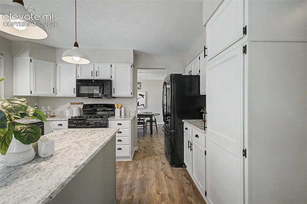 Image 21 of 49: Kitchen featuring white cabinetry with black hardware, stone countertops, b