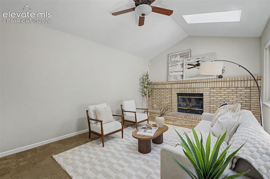 Image 28 of 49: Living area featuring a brick fireplace, vaulted ceiling, and skylight