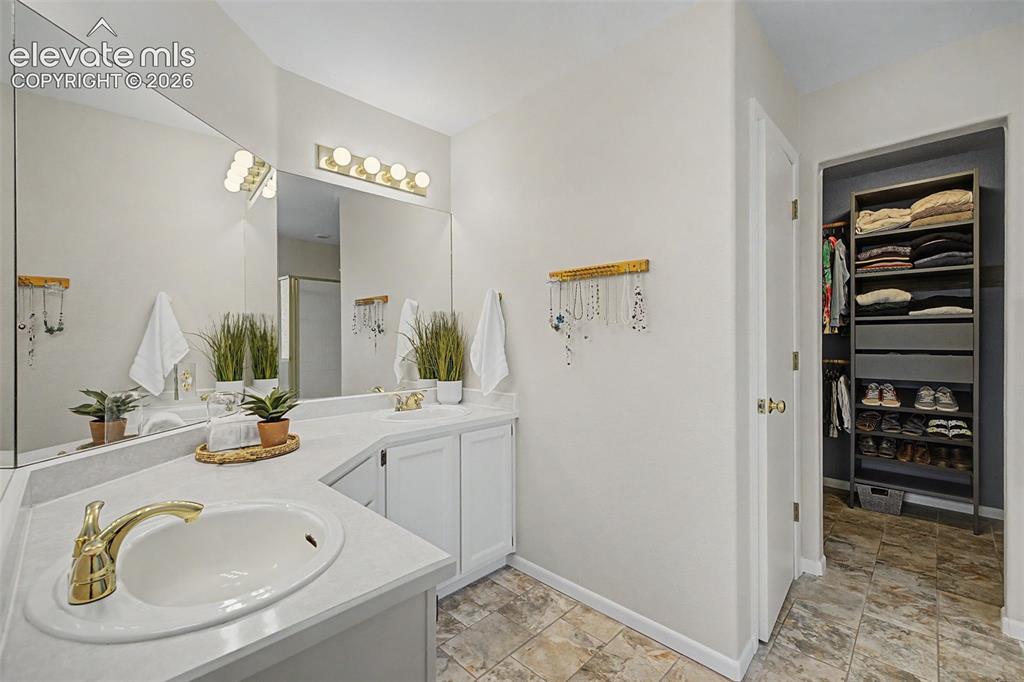 Image 34 of 49: Bathroom vanity featuring dual sinks with gold-finish faucets, white cabine