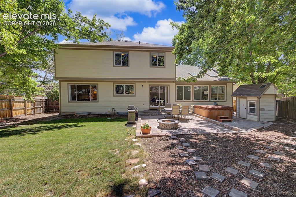 Image 43 of 49: Expansive rear yard featuring a stone patio, built-in hot tub, and a stone