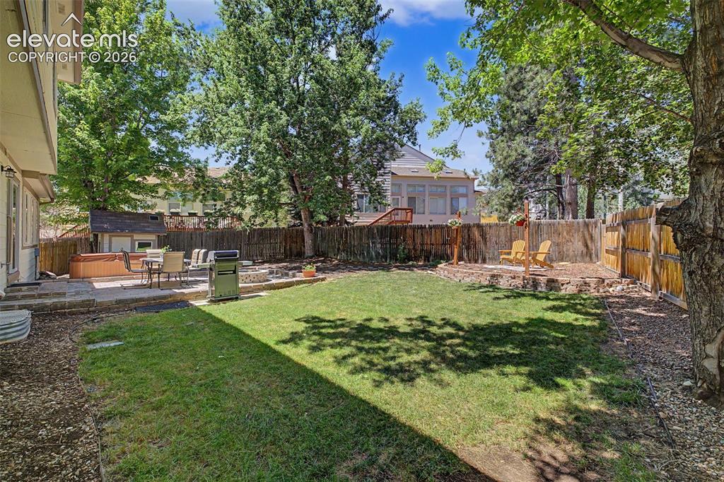 Image 45 of 49: Expansive backyard featuring a manicured lawn, stone patio, and wood privac