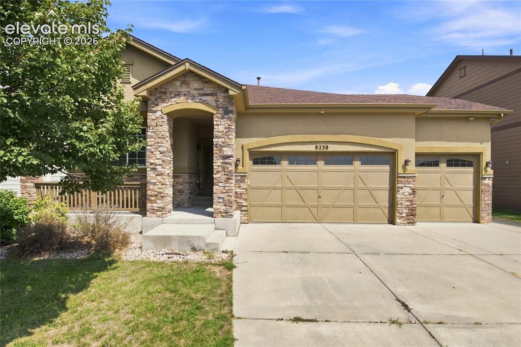 Caption: Stucco exterior with stone accents, covered front entry, attached two-car garage, and a concrete dri