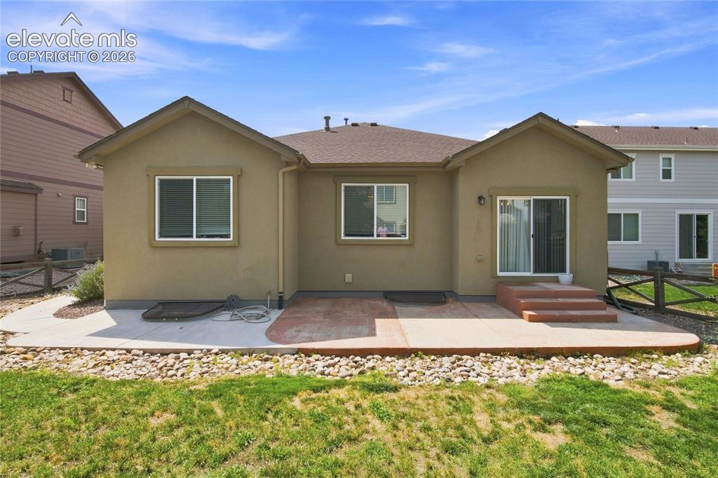 Image 18 of 18: Stucco exterior with multiple windows, featuring a concrete patio with a ti