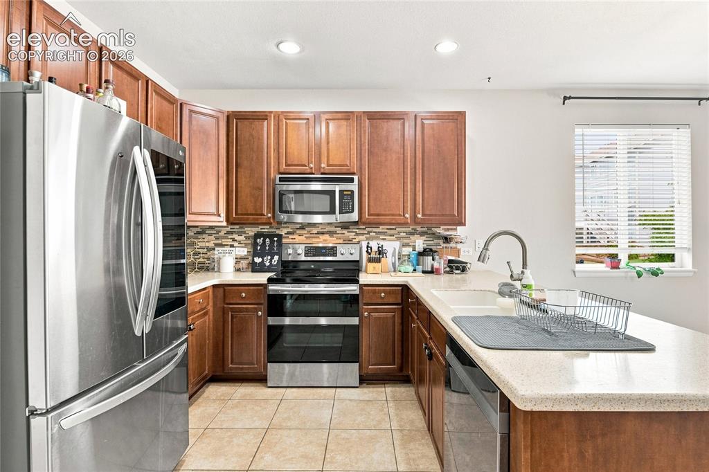 Image 5 of 18: U-shaped kitchen with wood cabinetry, light-toned countertops, tile floorin