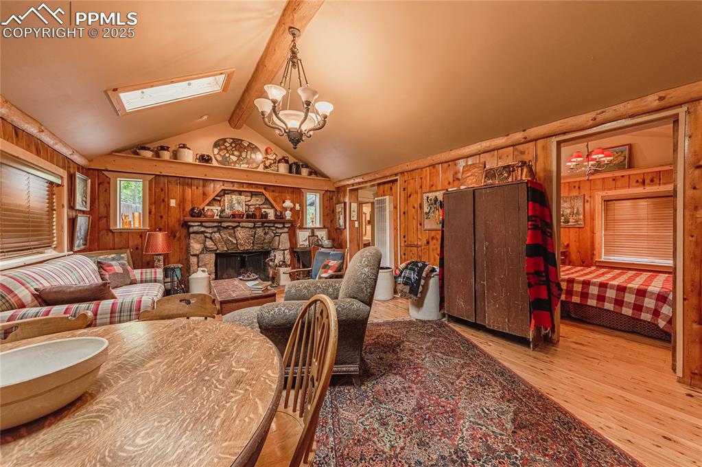 Image 4 of 23: Dining area with wooden walls, a chandelier, a stone fireplace, wood finish