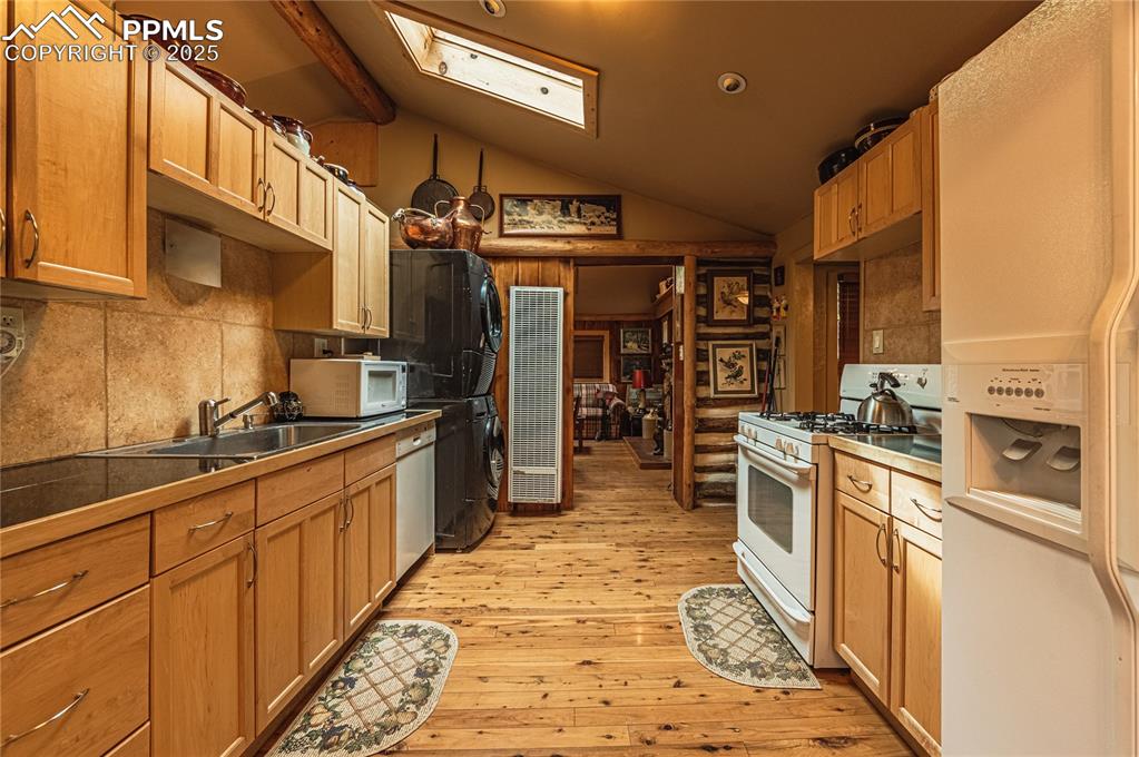 Image 8 of 23: Kitchen with decorative backsplash, white appliances, a skylight, vaulted c