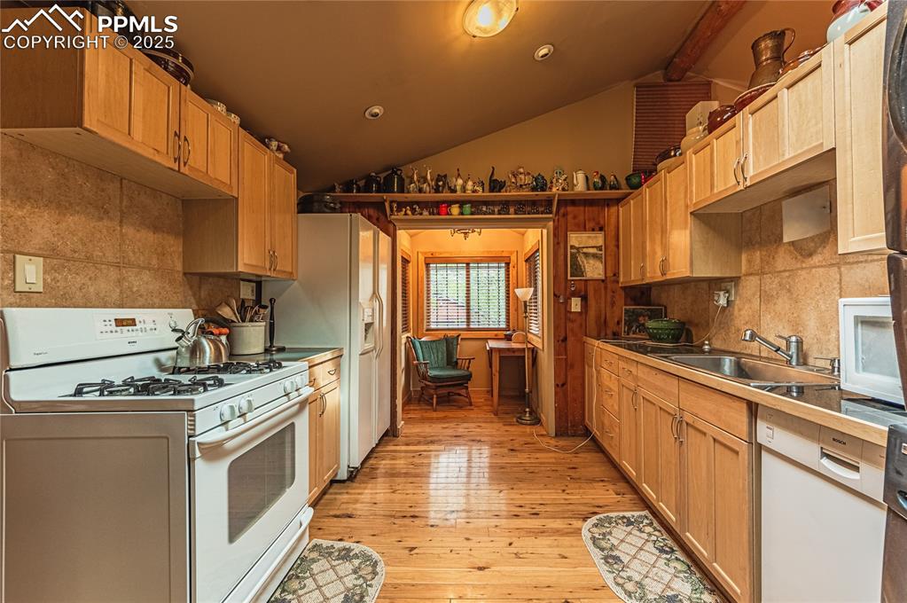 Image 9 of 23: Kitchen with white appliances, lofted ceiling, backsplash, light wood-type