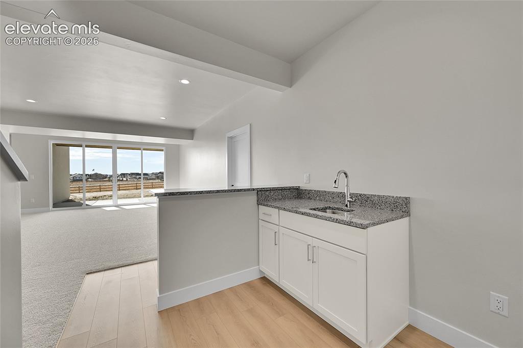 Image 25 of 35: Built-in wet bar featuring white cabinetry, a granite countertop, and a sta