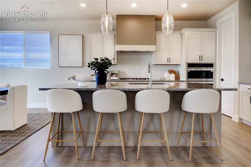 Image 7 of 35: Kitchen featuring a large central island with a stone countertop, white sha