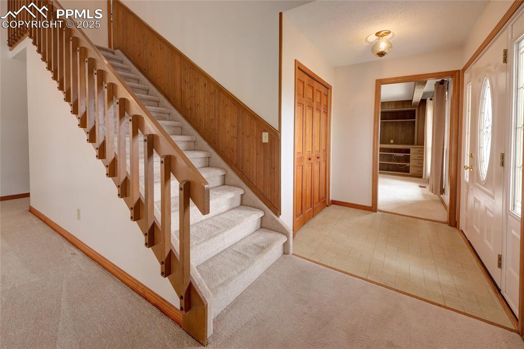 Image 4 of 48: Entryway featuring light colored carpet, wooden walls, stairway, and basebo