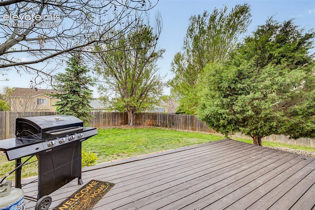 Image 16 of 45: Spacious backyard featuring a large deck, a manicured lawn, and mature tree