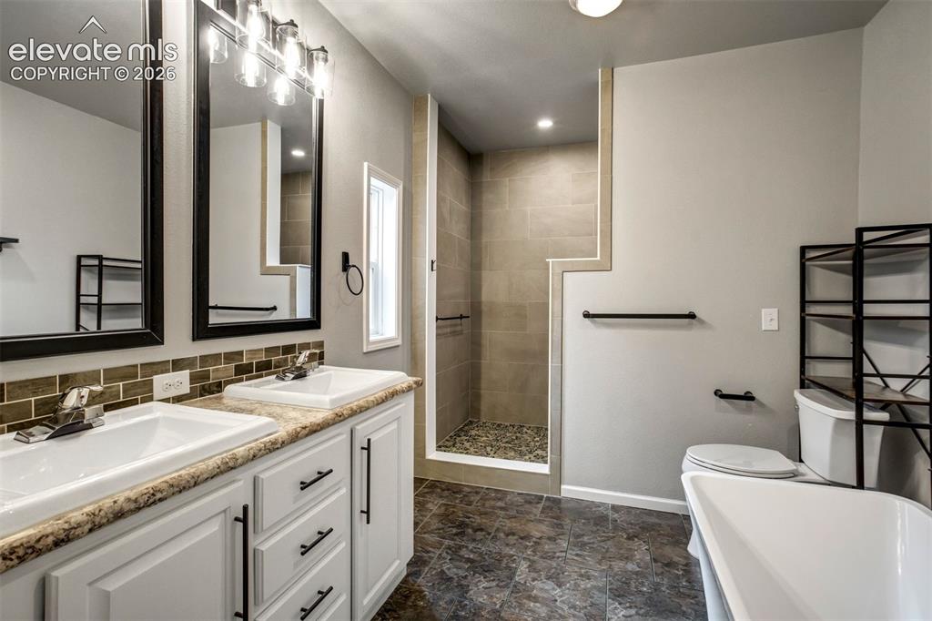 Image 18 of 48: Bathroom featuring a dual vanity with white cabinetry, a tiled backsplash, 