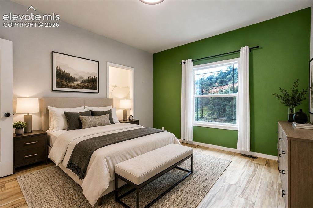 Image 22 of 48: Bedroom featuring a green accent wall, light wood-finish flooring, and a la