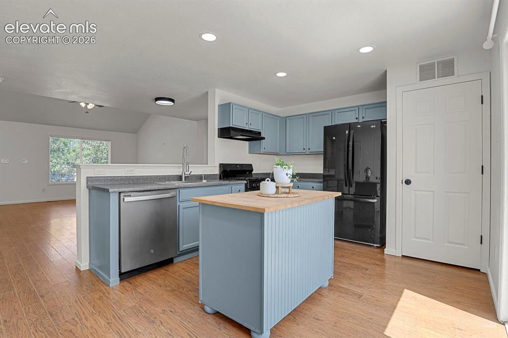 Image 14 of 49: Kitchen featuring light blue cabinetry, black appliances, wood-finish floor