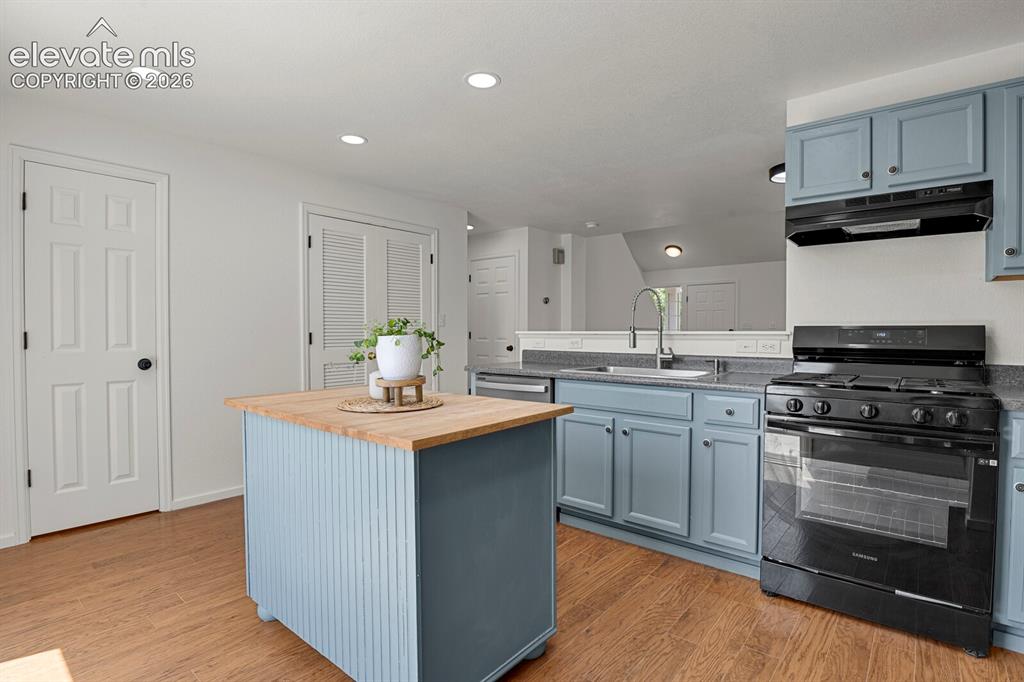 Image 15 of 49: Kitchen featuring light blue cabinetry, speckled countertops, a black gas r