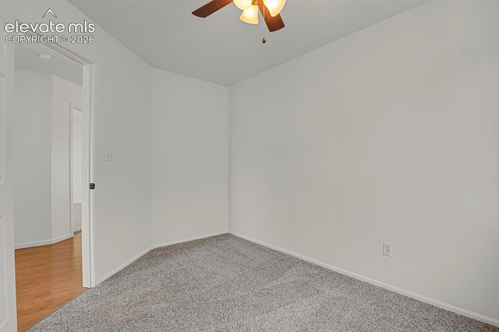 Image 31 of 49: Carpeted room with white walls, a wood-finish ceiling fan, and white trim