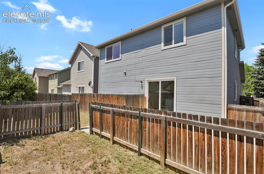 Image 39 of 49: Fenced backyard with wood privacy fencing, a sliding glass door, and vinyl