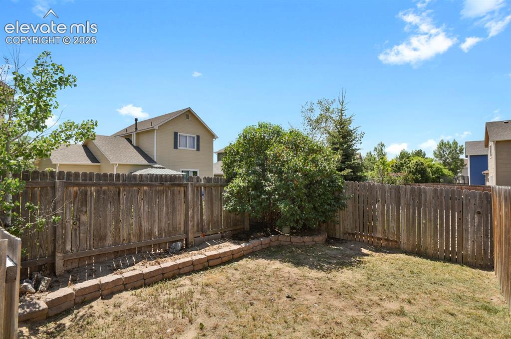Image 40 of 49: Fenced backyard featuring a wood privacy fence, a brick retaining wall, and