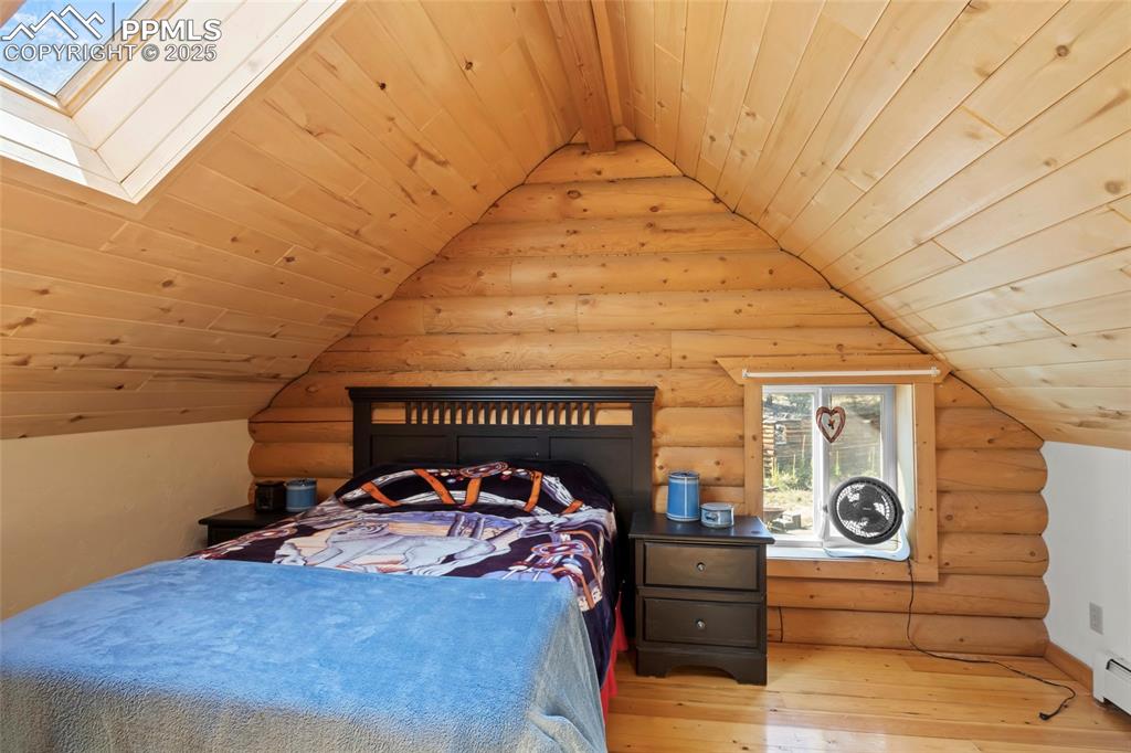 Image 18 of 33: Bedroom with wooden ceiling, rustic walls, a skylight, hardwood / wood-styl