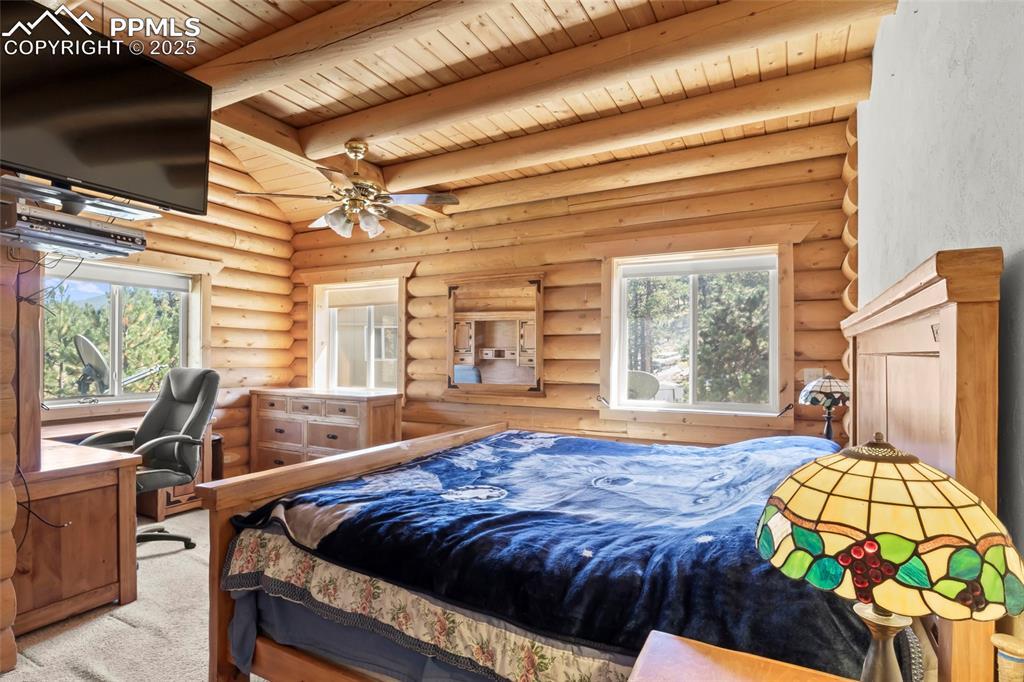 Image 8 of 33: Bedroom with log walls, a desk, multiple windows, carpet flooring, and a wo