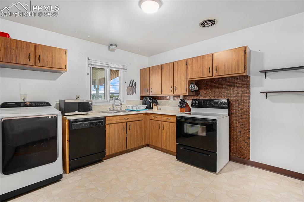 Image 13 of 30: Kitchen featuring washer / dryer, electric stove, black dishwasher, light c