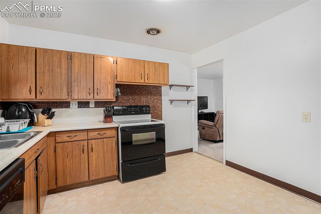 Image 14 of 30: Kitchen with black appliances, light countertops, brown cabinetry, and back