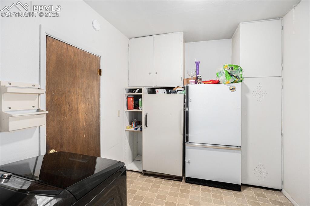 Image 15 of 30: Kitchen with light floors, freestanding refrigerator, and white cabinets