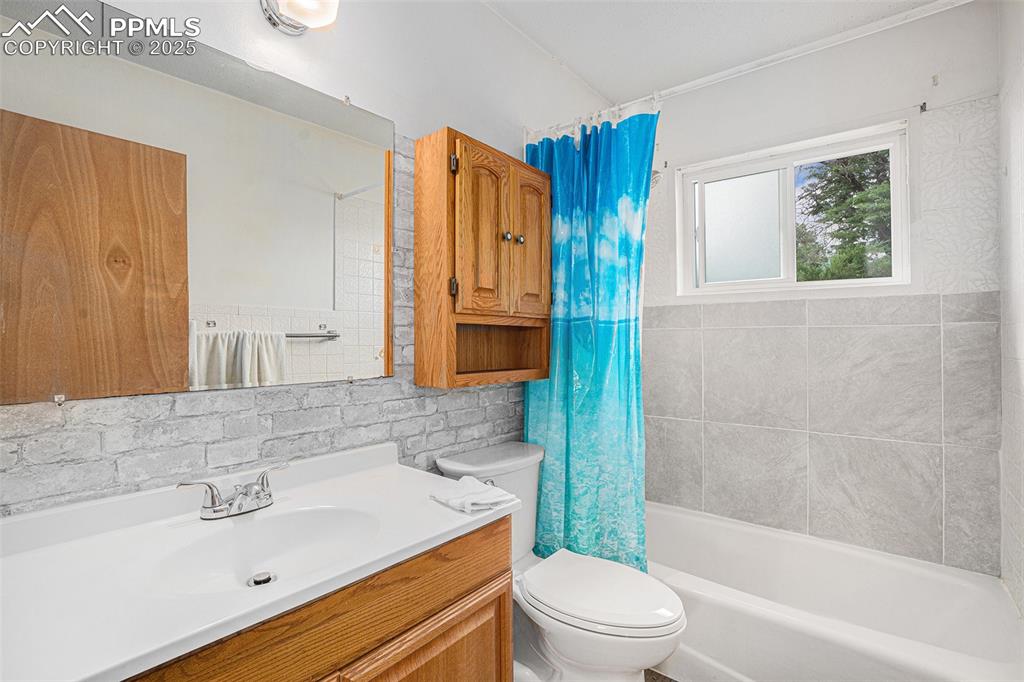 Image 22 of 30: Bathroom with vanity, shower / tub combo, tile walls, and backsplash