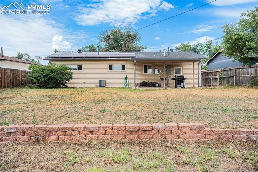 Image 24 of 30: Back of property featuring solar panels, a fenced backyard, and roof with s