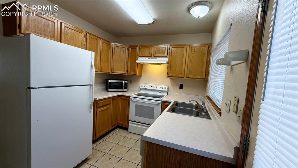 Image 3 of 16: Kitchen featuring white appliances, under cabinet range hood, a sink, light