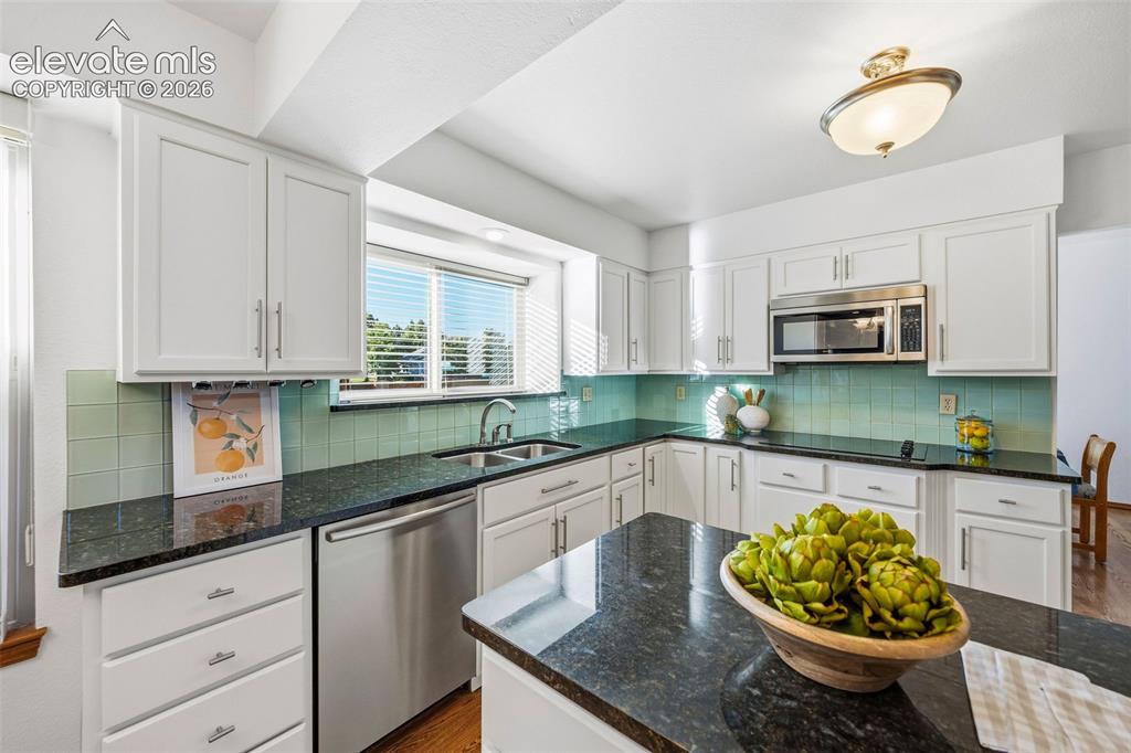 Image 17 of 49: Kitchen featuring white cabinetry, dark stone countertops, stainless steel 