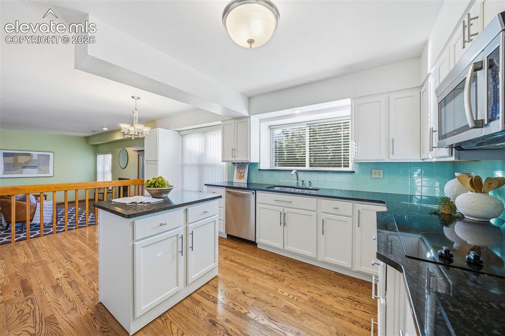 Image 18 of 49: Kitchen featuring white cabinetry, dark stone countertops, wood-finish floo