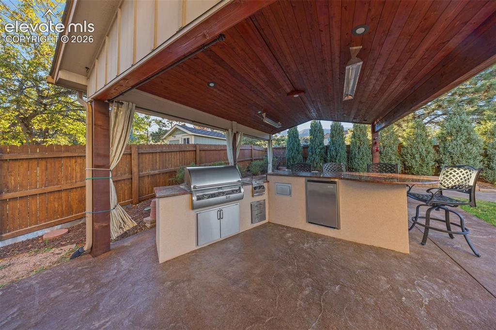 Image 38 of 49: Covered outdoor kitchen featuring a wood-plank ceiling, stamped concrete fl