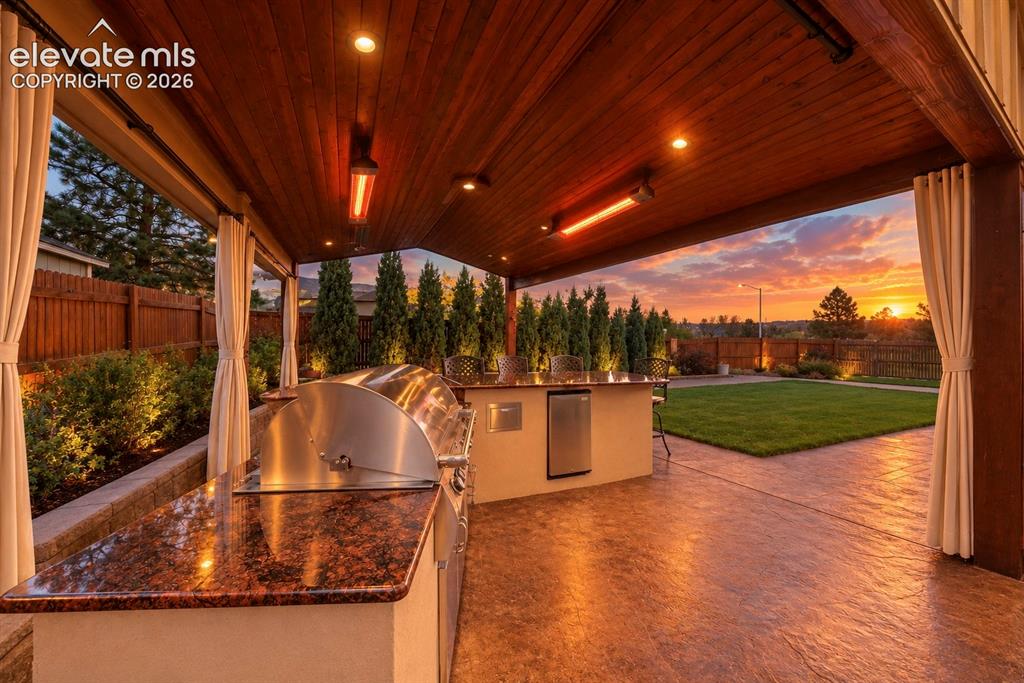 Image 40 of 49: Covered outdoor kitchen featuring a stone-finish countertop, built-in stain