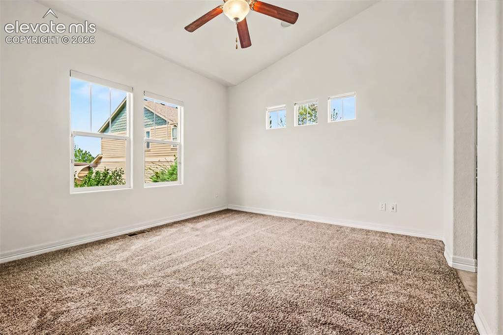 Image 12 of 44: Primary bedroom features vaulted ceiling and windows overlookiing the back