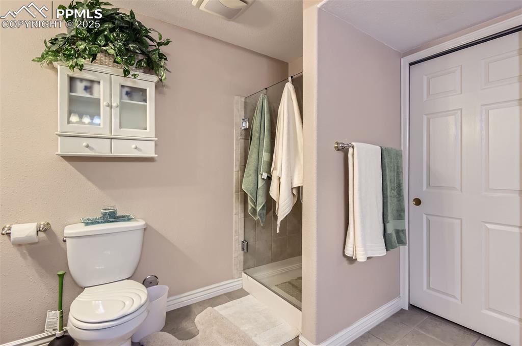 Image 27 of 28: Bathroom with tile patterned floors, toilet, and a shower with shower door