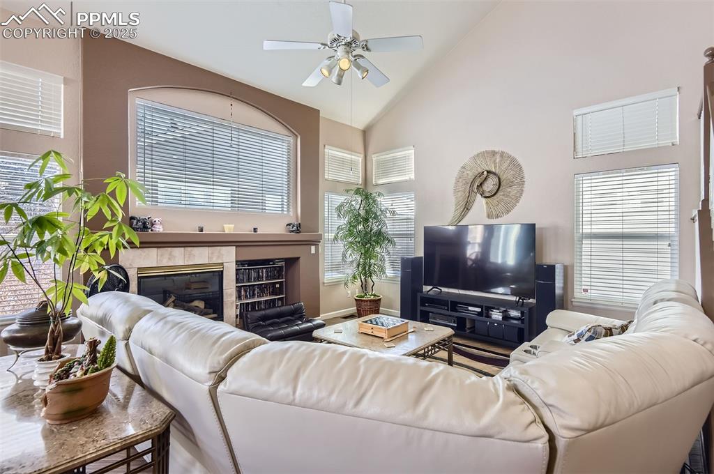 Image 7 of 28: Living room with a tiled fireplace, ceiling fan, and high vaulted ceiling