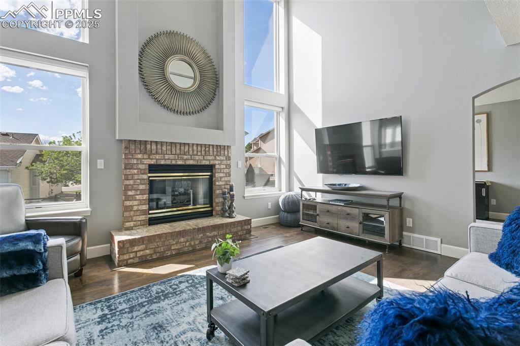 Image 20 of 50: The cozy gas fireplace is framed by four large windows! Roller shades are r