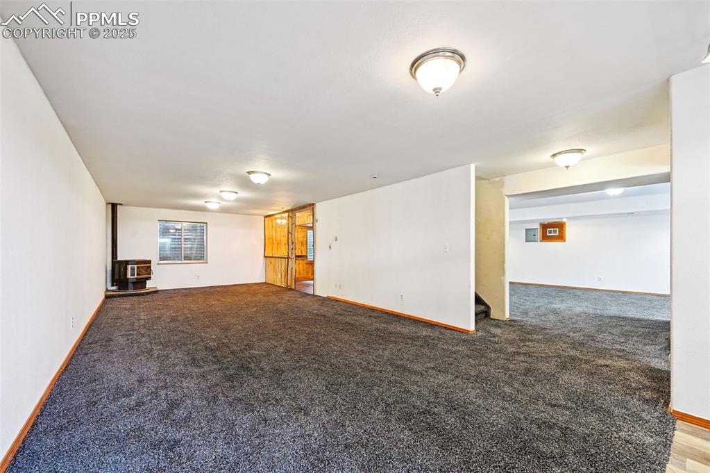 Image 27 of 50: Unfurnished living room featuring a wood stove, carpet, and stairway