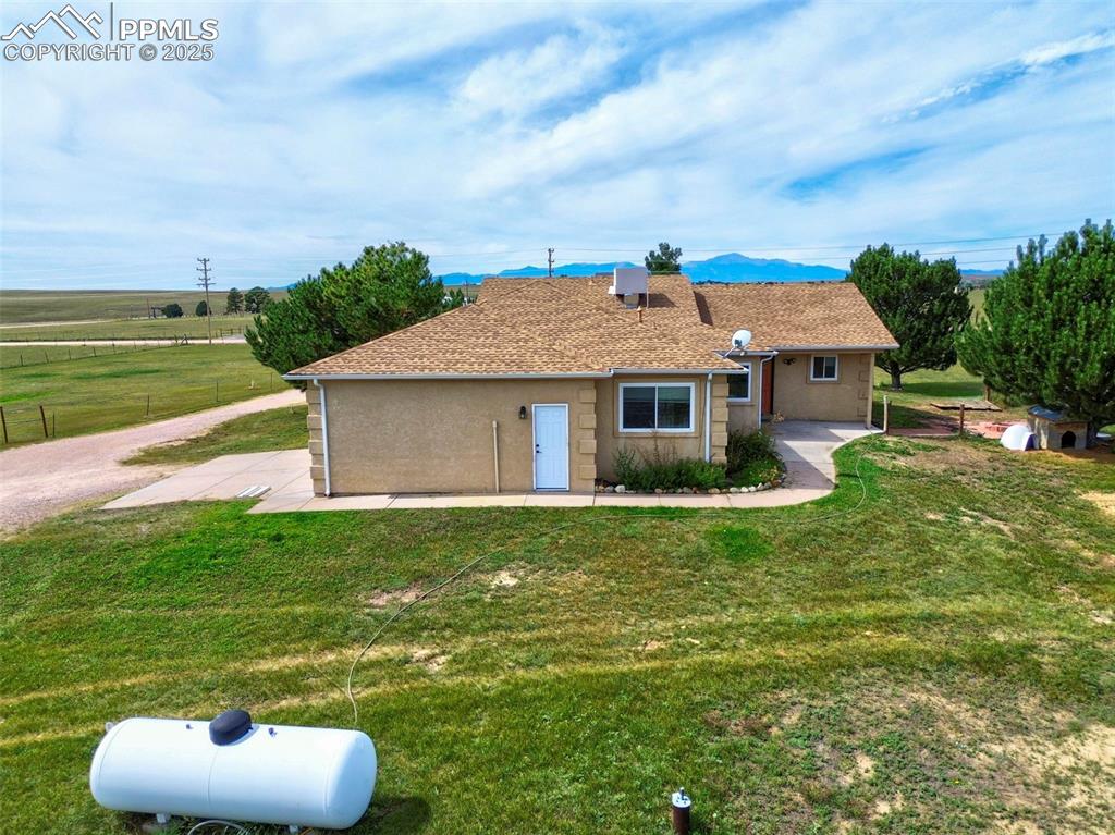 Image 42 of 50: Rear view of property featuring roof with shingles, a lawn, and a mountain