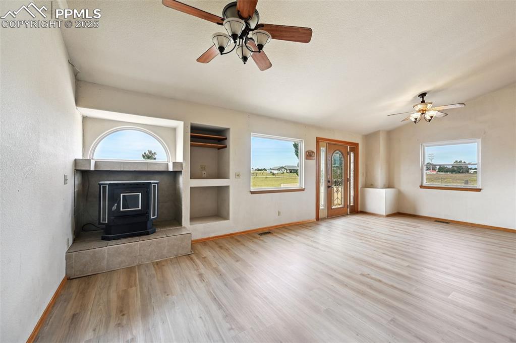 Image 7 of 50: Unfurnished living room with a wood stove, built in shelves, ceiling fan, l