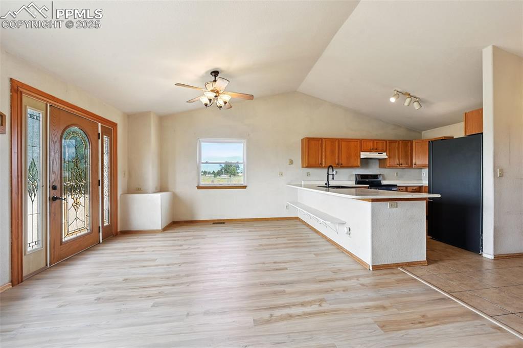 Image 8 of 50: Kitchen with light countertops, freestanding refrigerator, brown cabinets,