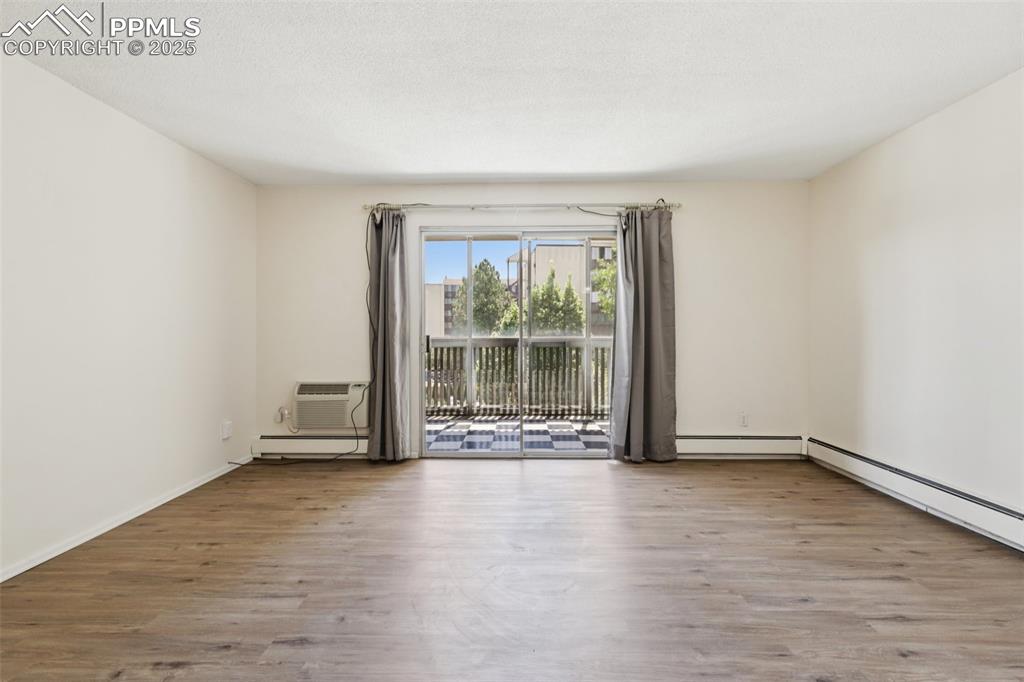 Image 8 of 25: Unfurnished room with wood finished floors, a baseboard radiator, and a wal