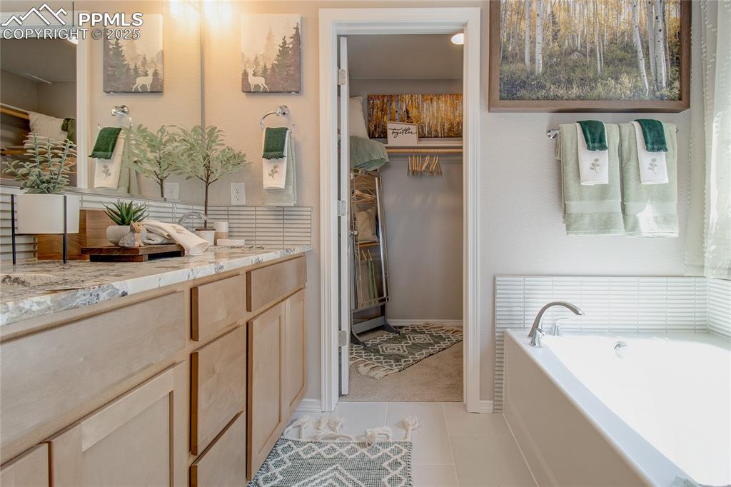 Image 15 of 27: Bathroom with a garden tub, a spacious closet, vanity, and light tile patte