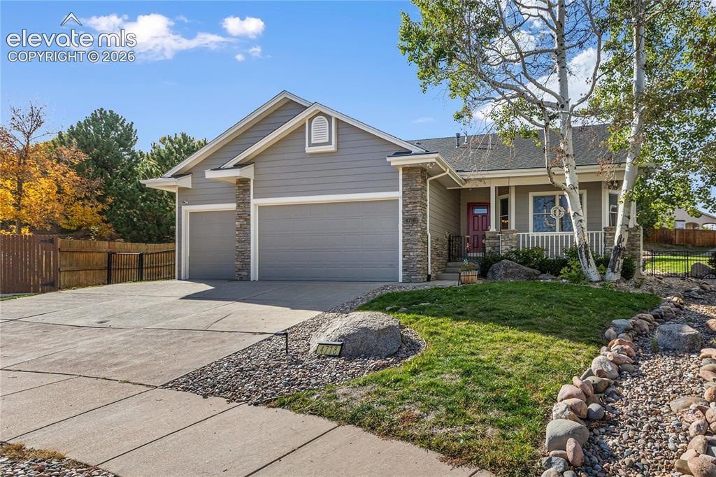 Caption: Exterior featuring a gray siding facade, stone accents, two-car garage, covered porch, and mature tr