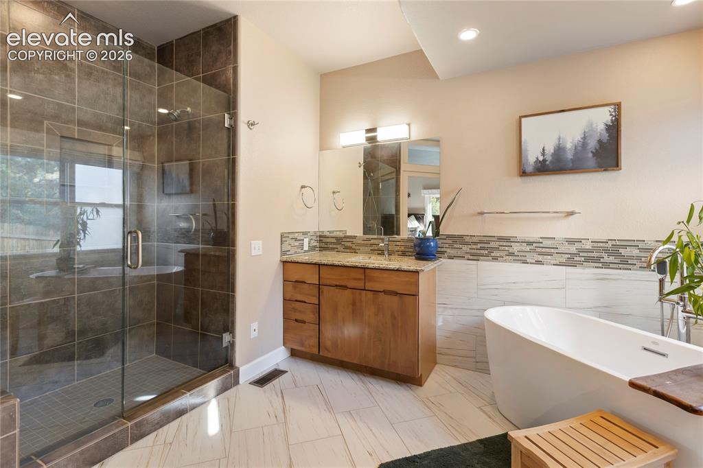 Image 10 of 38: Glass-enclosed shower with dark tile surround, freestanding soaking tub, wo