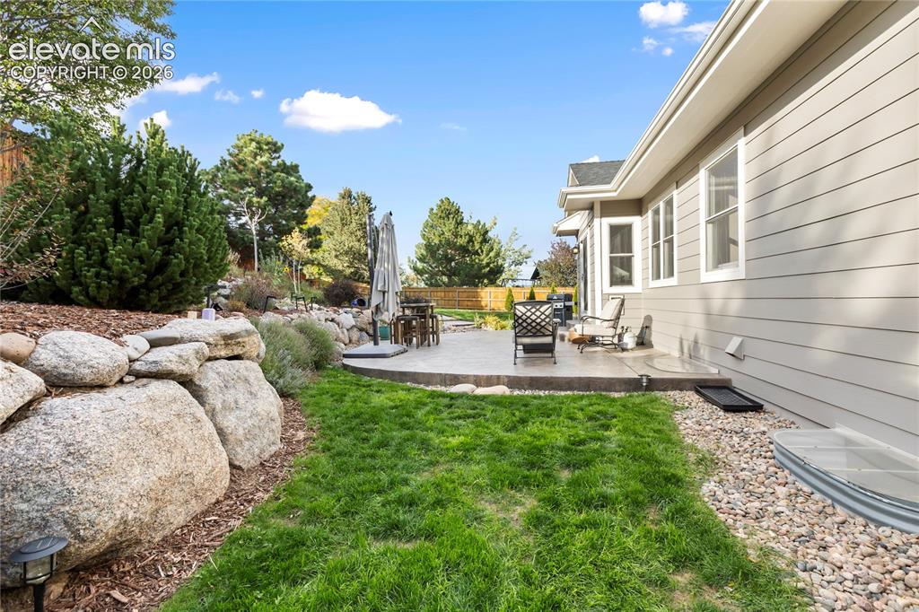 Image 13 of 38: Expansive patio with concrete surfacing, surrounded by a rock retaining wal